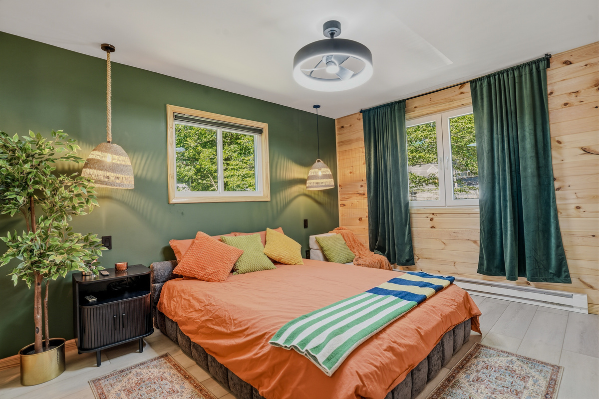  Queen bedroom with green accent walls, wood paneling, ceiling fan, and natural light