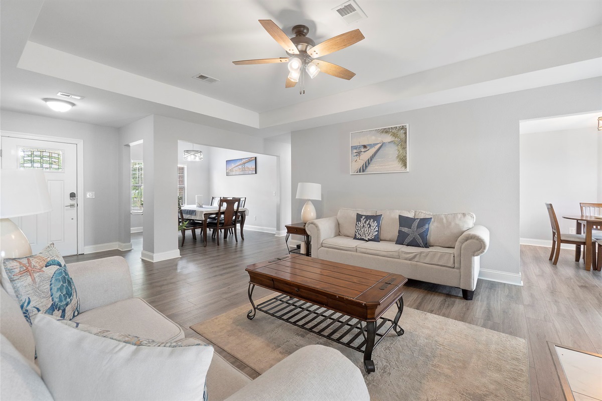 This open-concept living room blends soft coastal tones with modern finishes. The clean layout, elegant tray ceiling, and tasteful décor create a warm and welcoming atmosphere