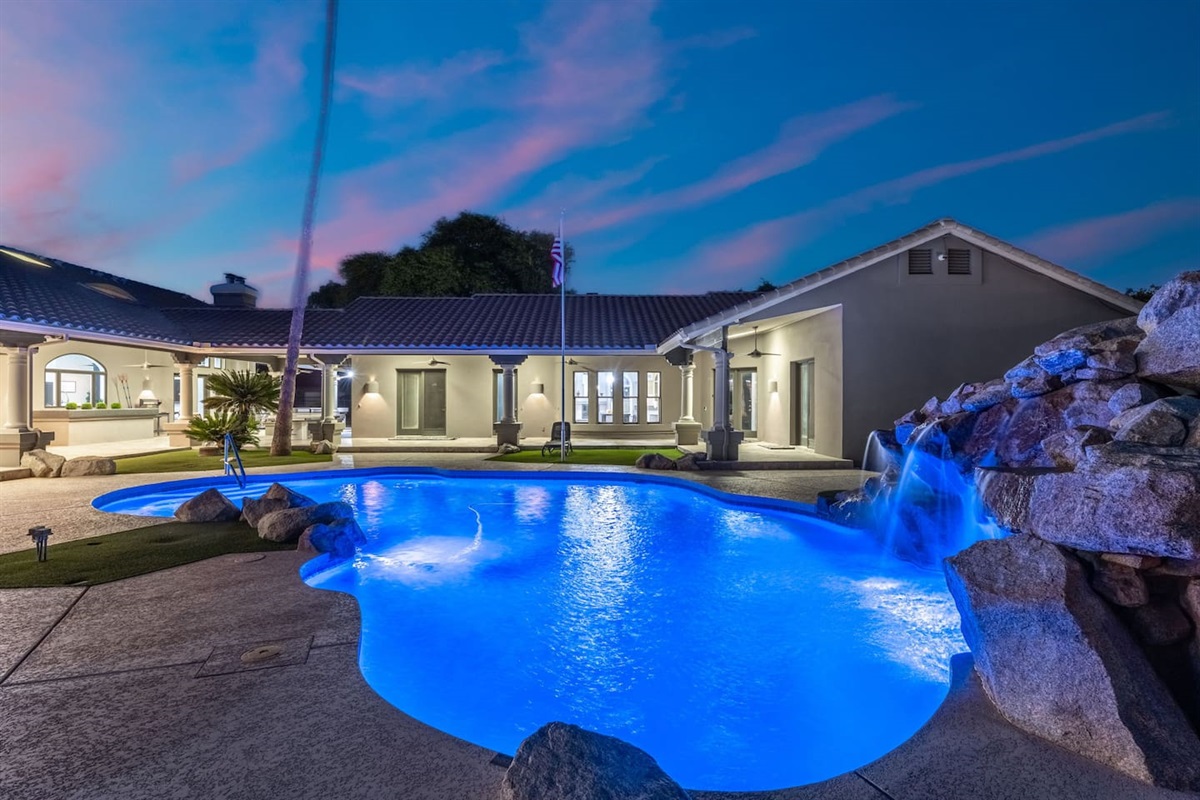 Mesmerizing poolside evenings with glowing waters and a cascading rock waterfall—pure backyard luxury.

