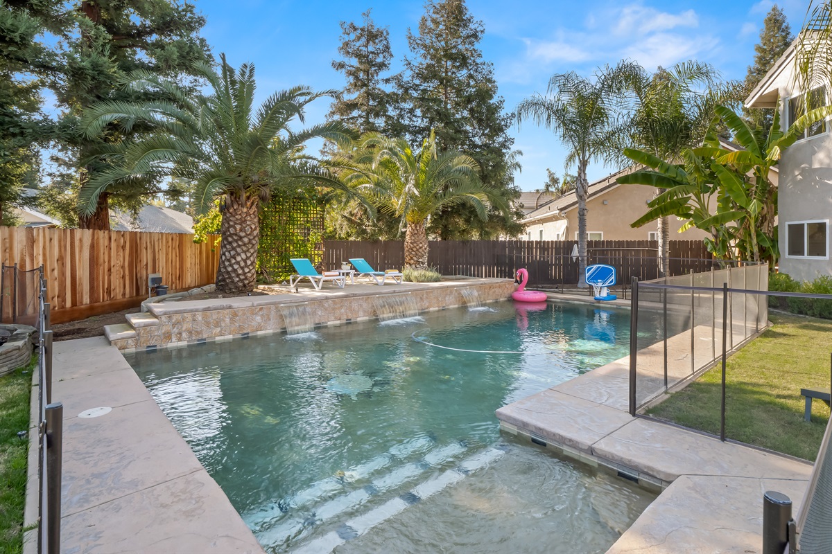 Private backyard oasis featuring a sparkling pool with waterfalls, lounge chairs, and tropical landscaping.