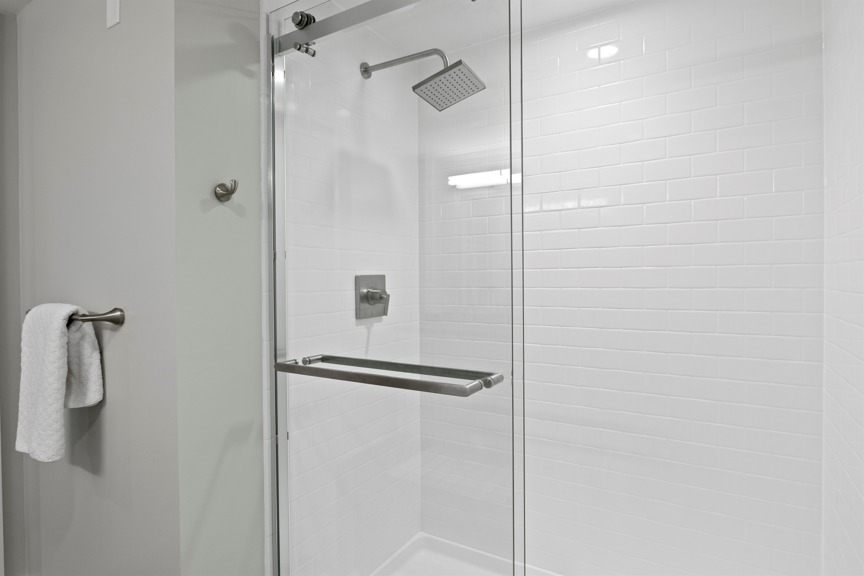 Glass-enclosed shower with modern hardware and soothing white tile creates a bright, luxurious feel.