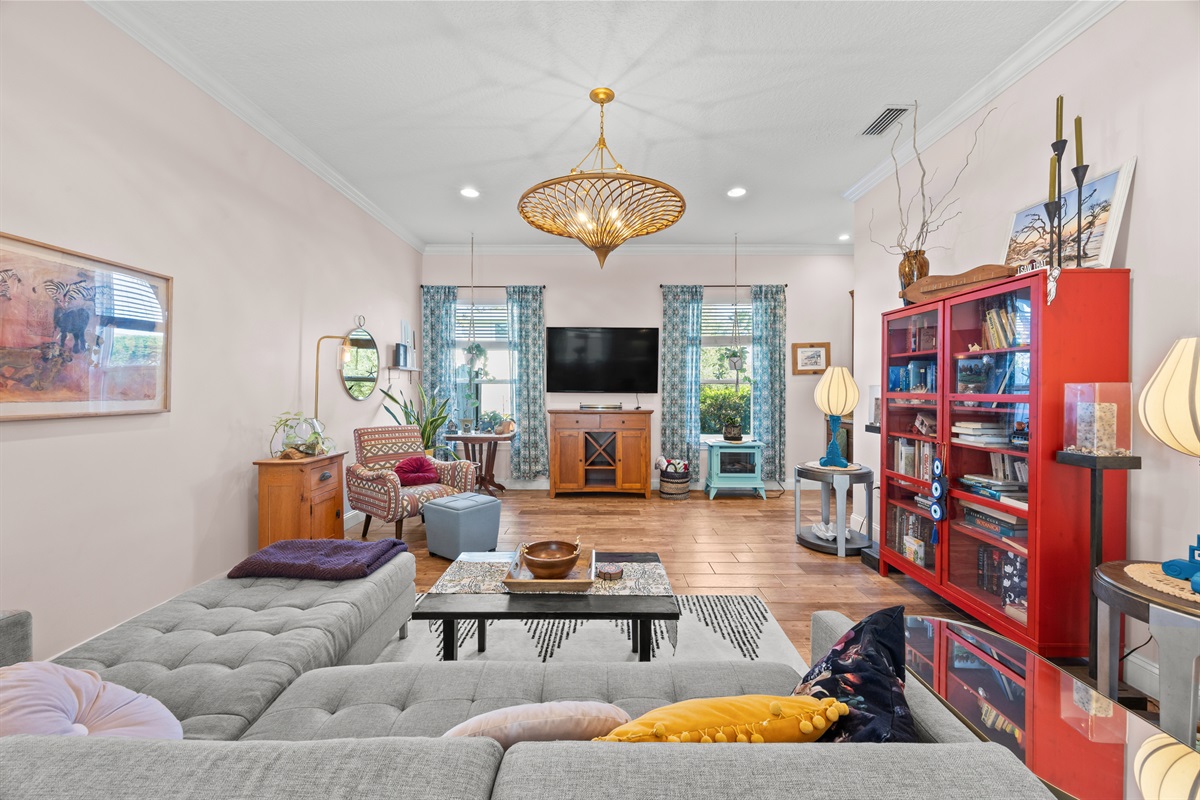 Colorful living room with gray sectional, eclectic décor, and red bookshelf in Jacksonville Beach family‑friendly rental home.