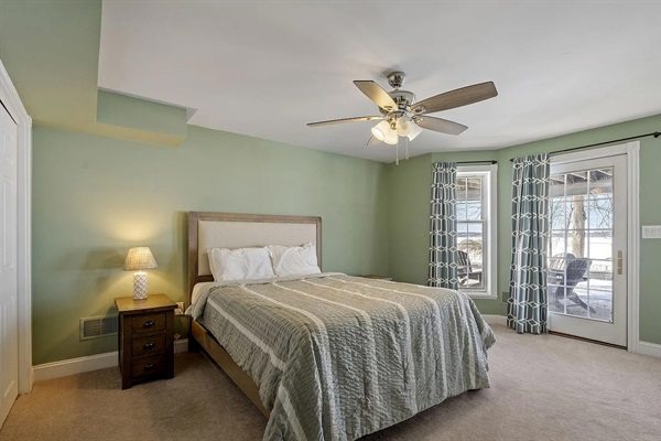 A peaceful ground-floor lakeview retreat with a queen bed, oversized windows overlooking the water, connected bathroom, TV ,desk+chair, and direct access to the outdoor patio and firepit area.