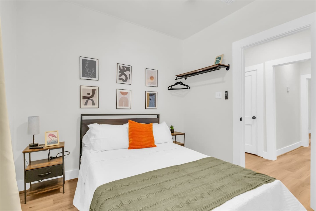Queen bedroom with queen bed, exposed closet with hangers, room darkening shades and a TV.