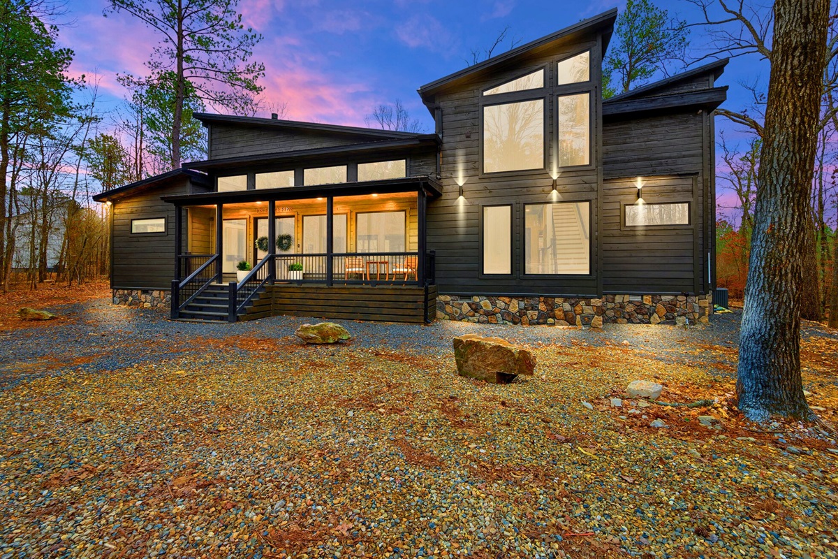 A wide view of the cabin shows off its modern architecture and inviting glow as the sun sets.