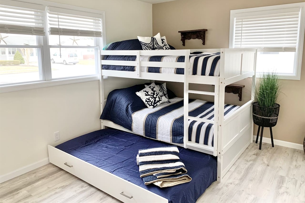 Perfect for kids or groups, this bright room features a white wooden bunk bed with nautical striped bedding and a pull-out trundle. Large windows fill the space with light, creating a cheerful spot for guests to rest.