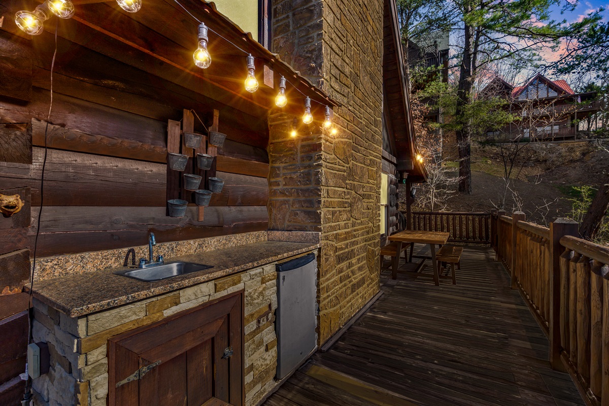 Enjoy outdoor dining with a fully equipped outdoor kitchen featuring a sink, counter space, and mini fridge; perfect for grilling, prepping, and gathering around the picnic table for meals in the fresh mountain air.