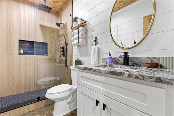 Luxury shower experience with a large rain shower head, standard shower head, three body jets, and a handheld sprayer. Sleek natural stone vanity and modern fixtures make this spa-like bathroom a highlight of the home.