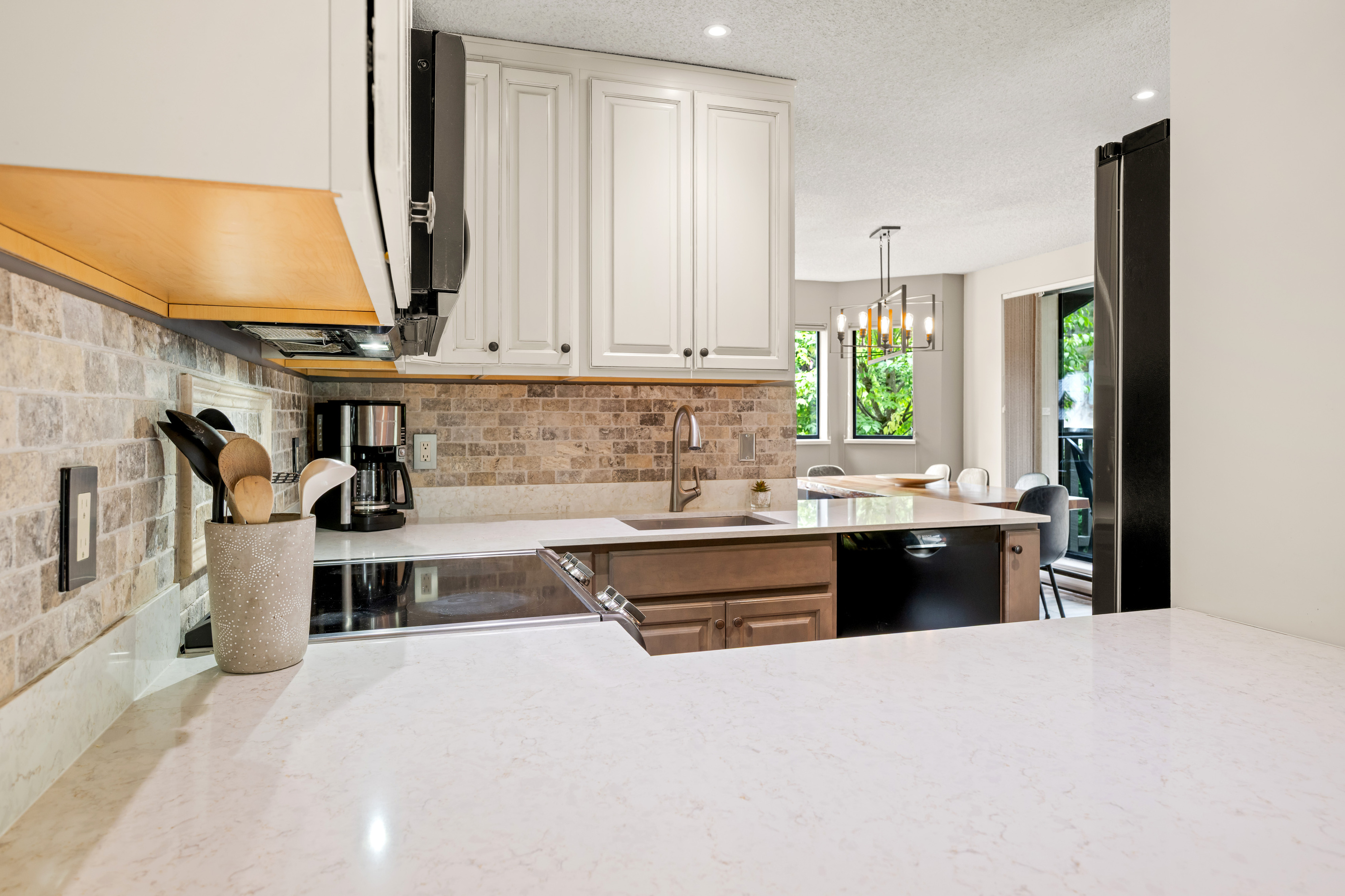 Kitchen with a stone backsplash and a 10-cup drip coffee maker, open to the dining room beyond.