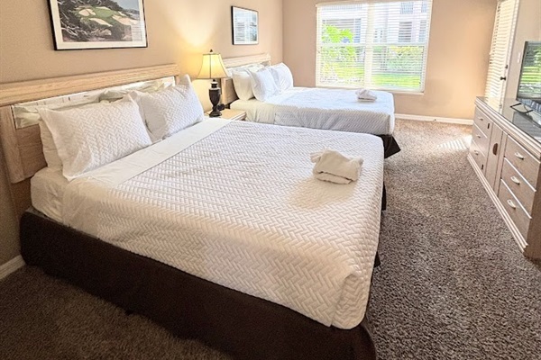 Spacious bedroom with two beds, dresser storage, ceiling fan, and a clean, relaxing setup.