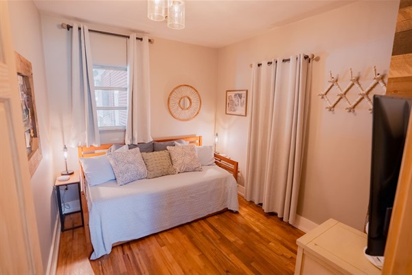 Cozy bedroom with a daybed and trundle, hardwood floors, soft lighting, and simple décor. A comfortable space ideal for kids or additional guests.