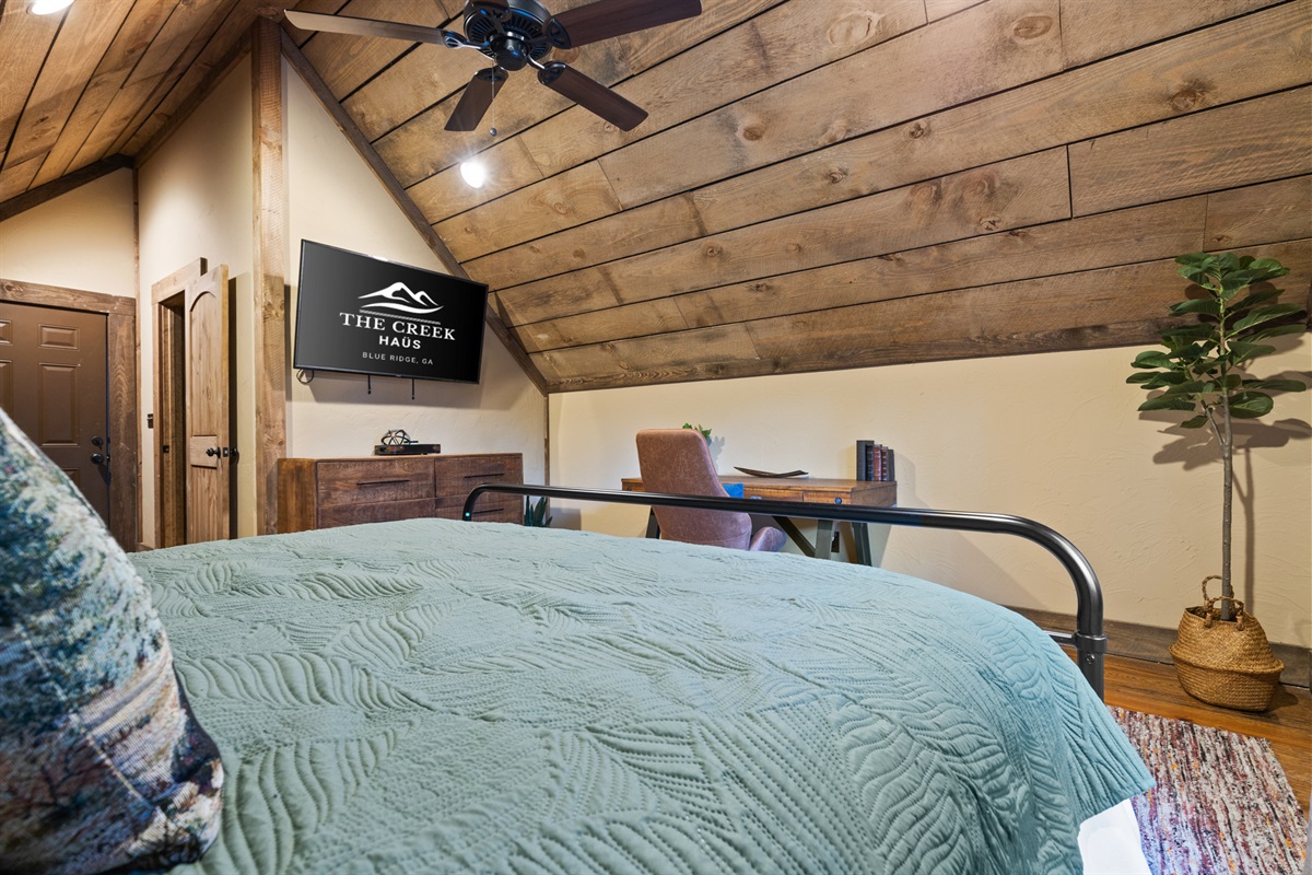 The private king suite above the garage features cozy furnishings, a smart TV, and a quiet desk nook, offering both comfort and privacy.