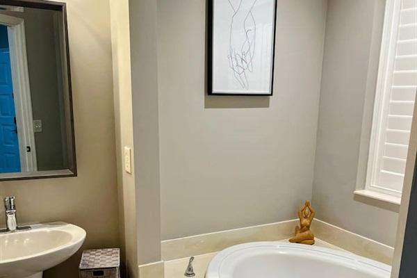 Bright bathroom with a soaking tub area, neutral finishes, and natural light from the window.