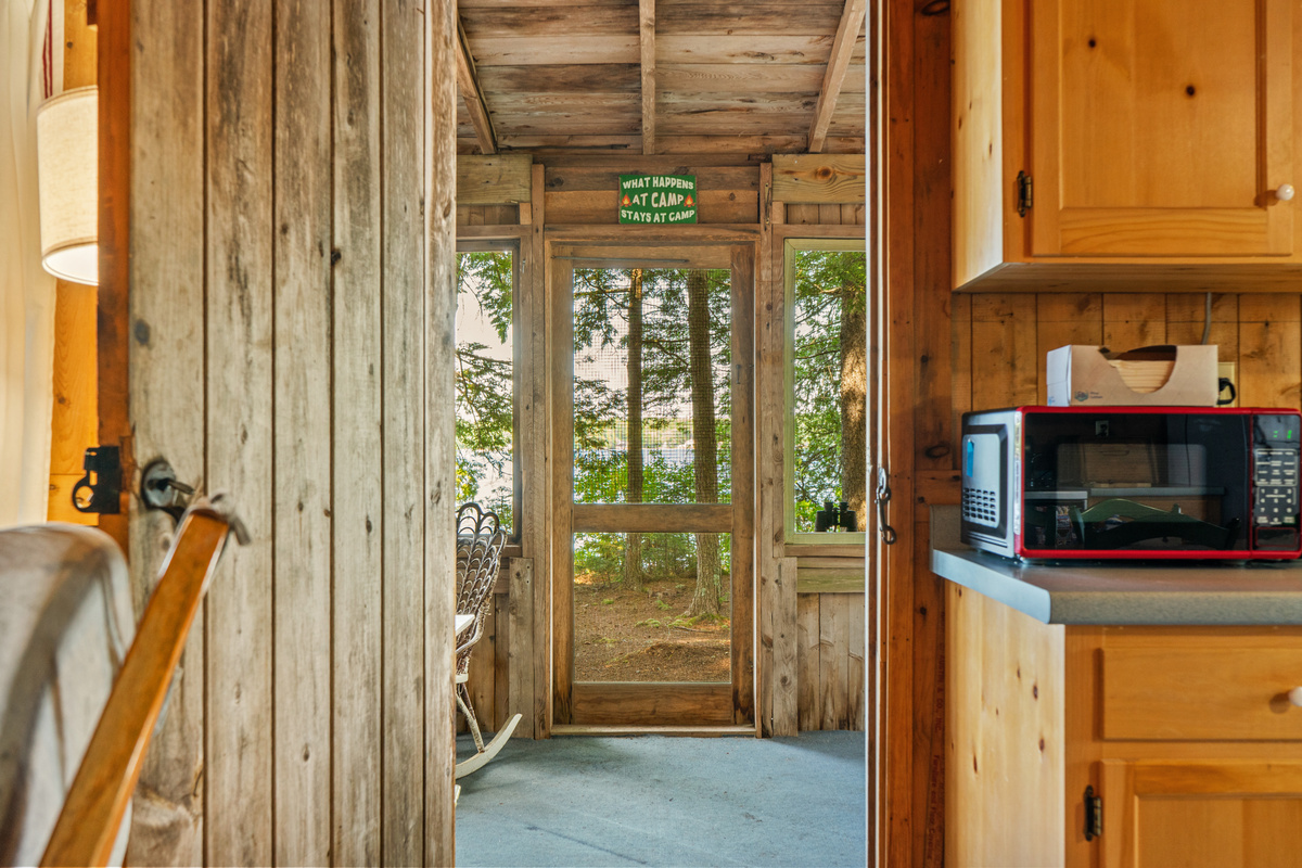 Scenic outward view at Loonrise Point! Looking from the main interior through the screened porch to pine trees and lake views beyond. Highlights our seamless indoor-outdoor camp connection on Beech Hill Pond in Otis, ME.