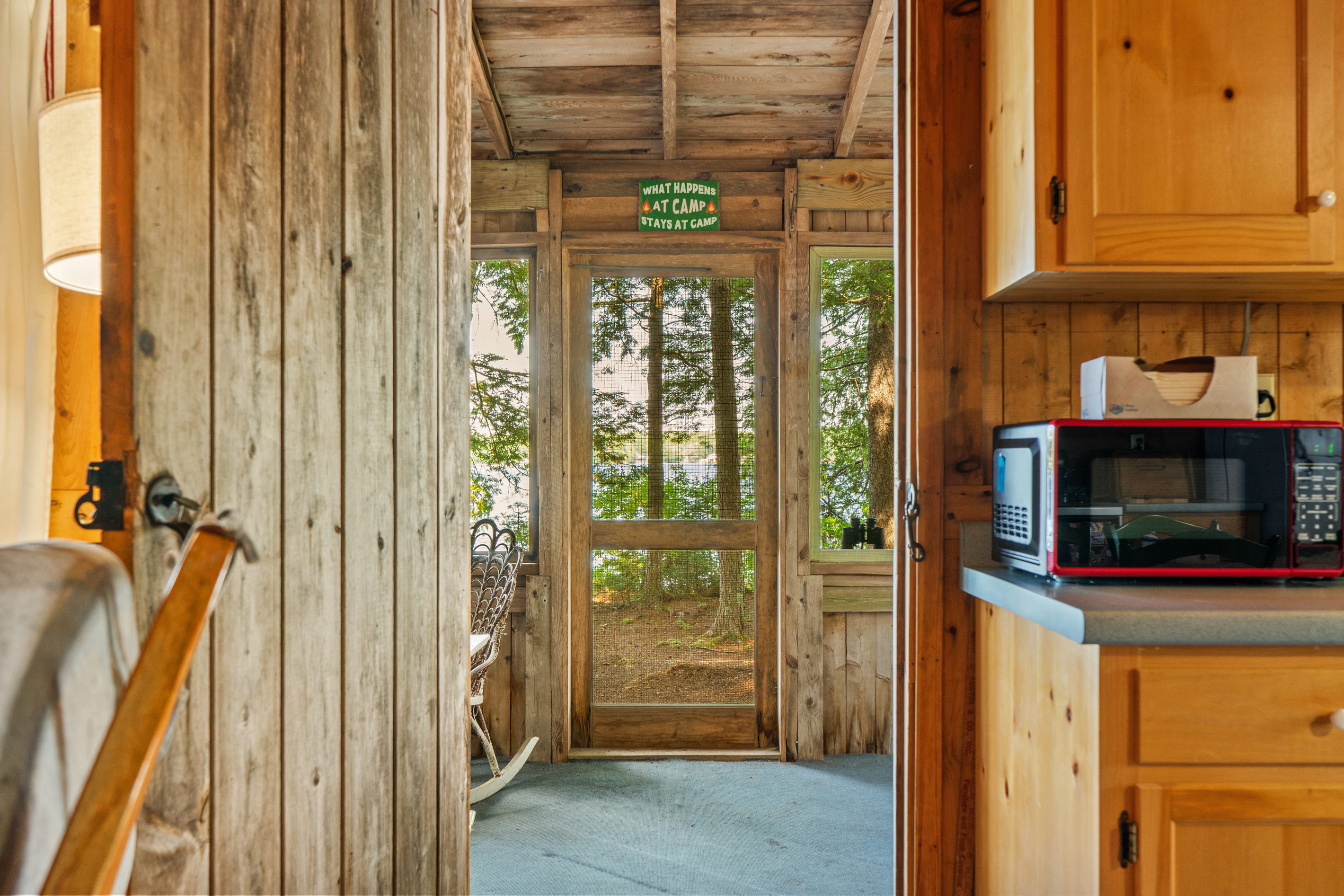 Scenic outward view at Loonrise Point! Looking from the main interior through the screened porch to pine trees and lake views beyond. Highlights our seamless indoor-outdoor camp connection on Beech Hill Pond in Otis, ME.