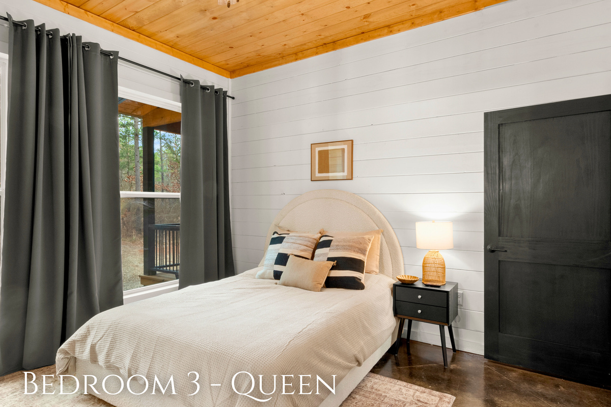 A charming queen-sized bed framed by large windows that draw in natural light and views of the serene outdoors.