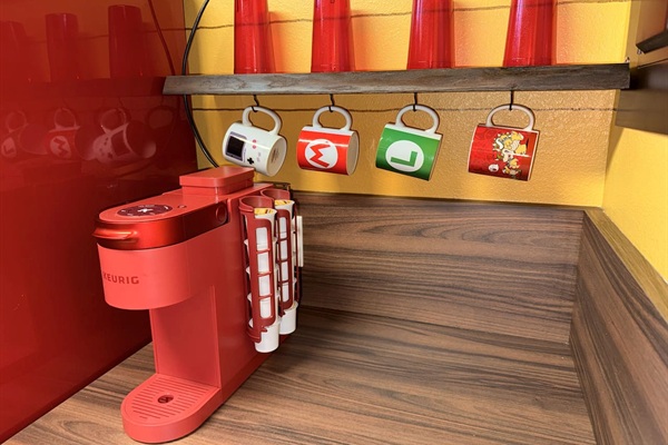 Convenient Keurig coffee maker at Mario's Mini Mansion in Clermont, FL! Mounted on the wall with colorful Mario-themed mugs (including power-up designs) hanging nearby—easy morning coffee for the whole family in our themed kitchen.