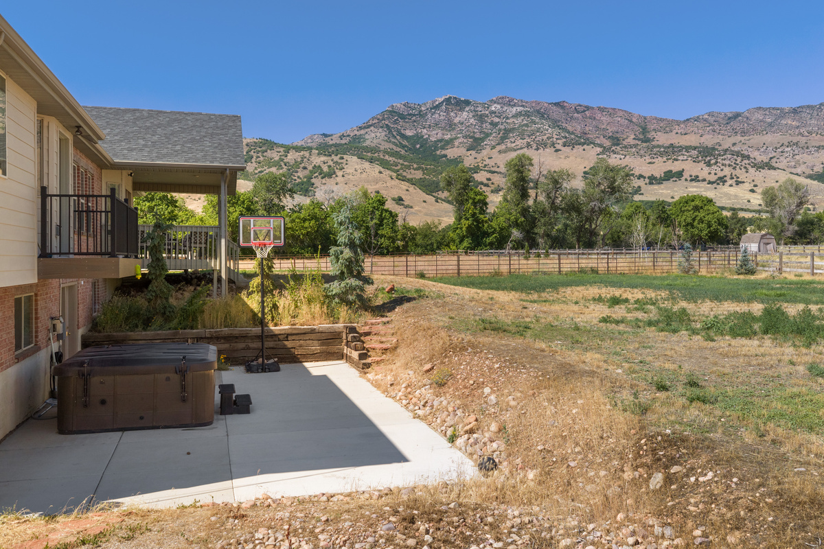The backyard combines open countryside, dramatic mountain scenery, a private hot tub, and a basketball hoop for a relaxed blend of leisure and recreation.
