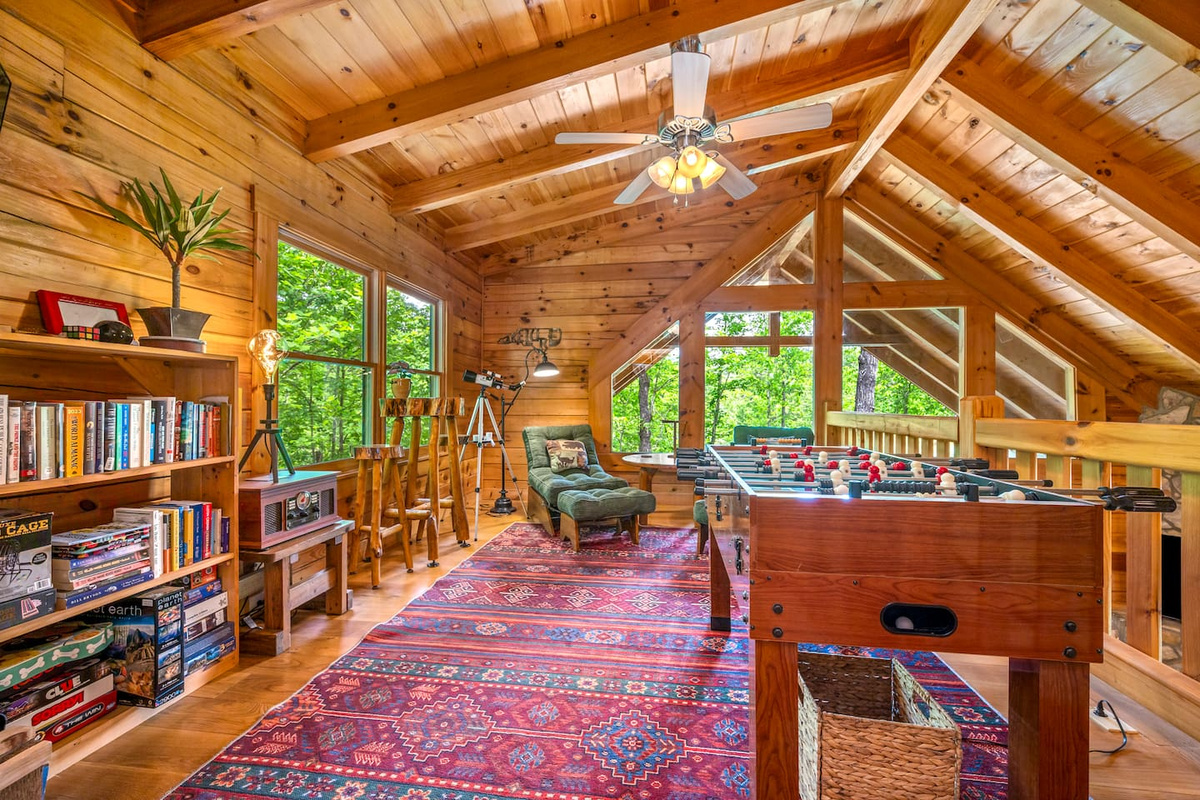 Loft game area with foosball table, reading nook, board games, and peaceful treetop views. The perfect upstairs retreat for family fun and relaxing cabin nights.