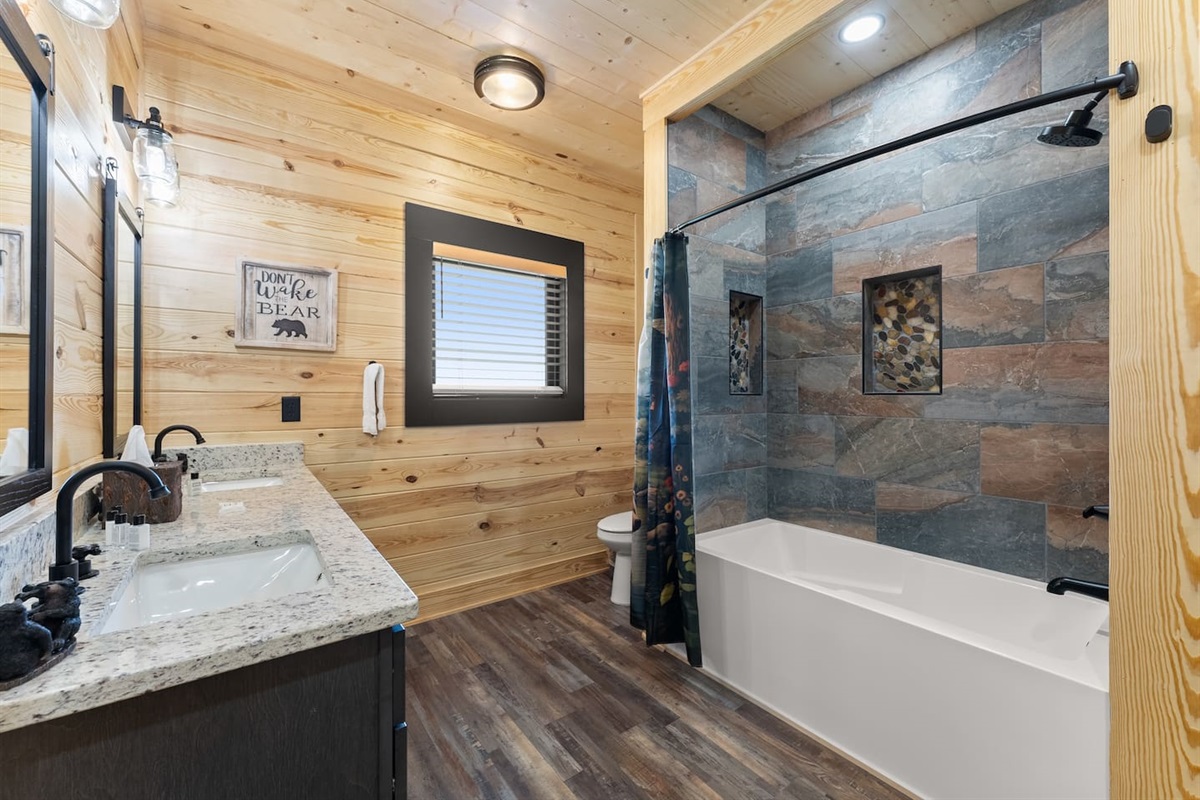 Rustic charm meets convenience in this third full bathroom, featuring a double vanity with granite counters and black fixtures.