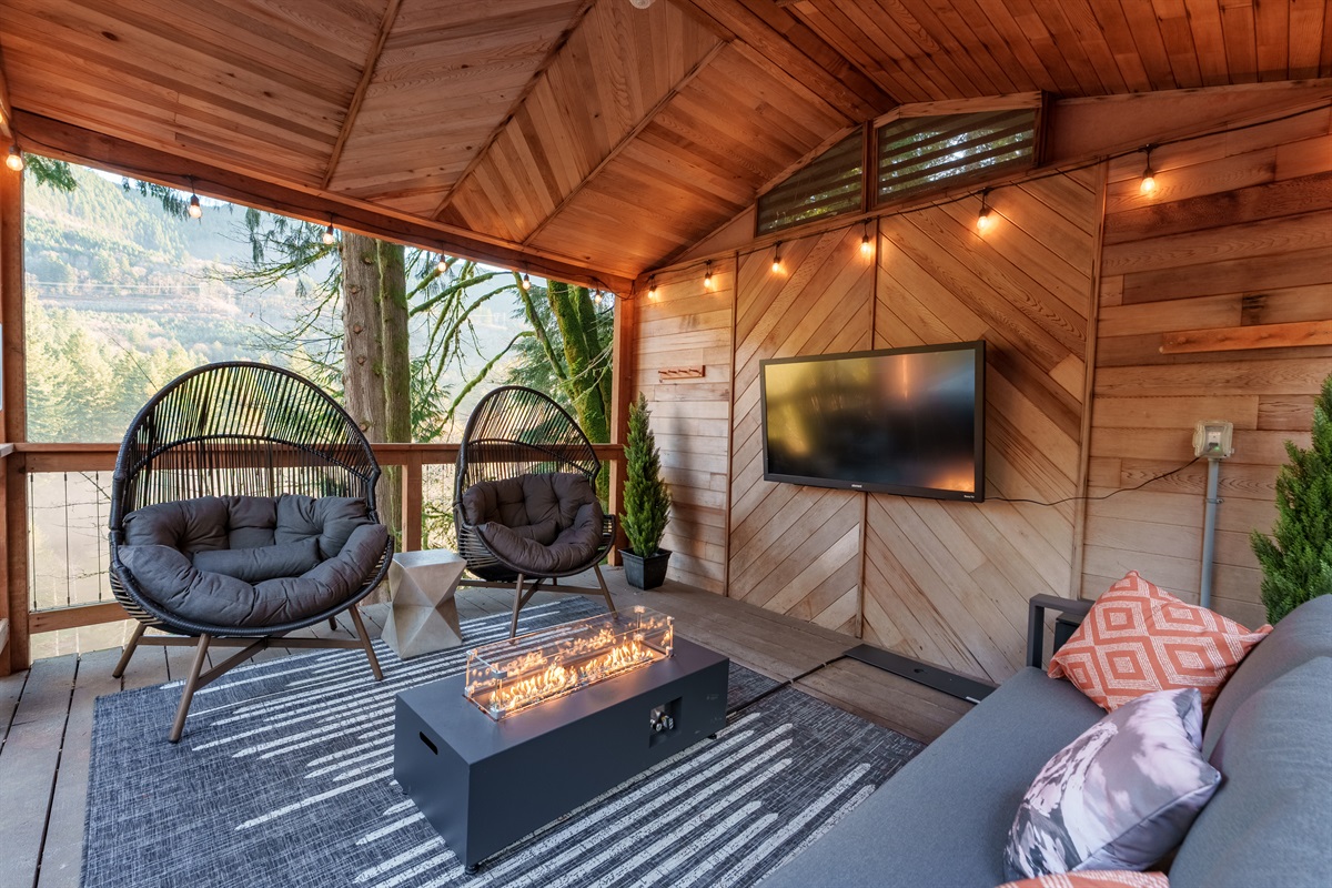 Settle into the covered deck lounge with cozy seating, a modern fire feature, and forest views—your perfect spot for movies, morning coffee, or unwinding after a day on the mountain.