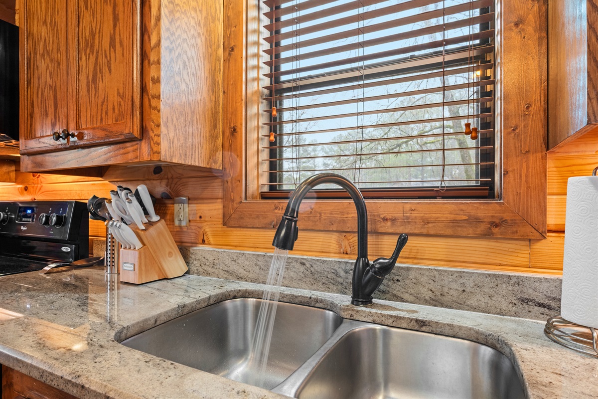 The kitchen sink area features rustic finishes and natural light that brighten the space and add to the cabin’s cozy charm.