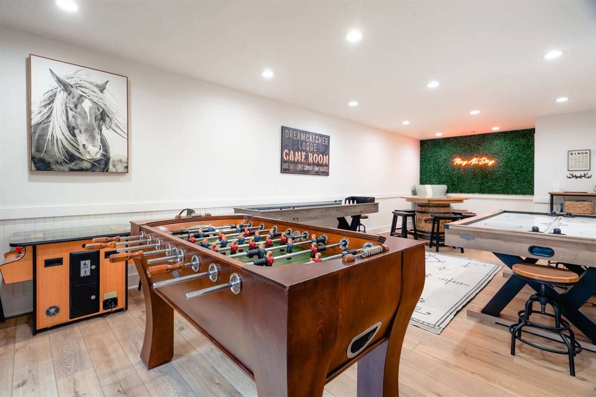 Game room with foosball, air hockey, shuffle board, arcade table, and game table with poker set and board games. 