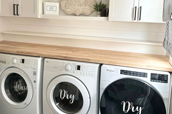This bright laundry room features high-efficiency washer and dryers with a spacious butcher block folding counter. This well-appointed area includes overhead storage and shelving, making it easy to enjoy fresh towels and linens during your beach vacation.