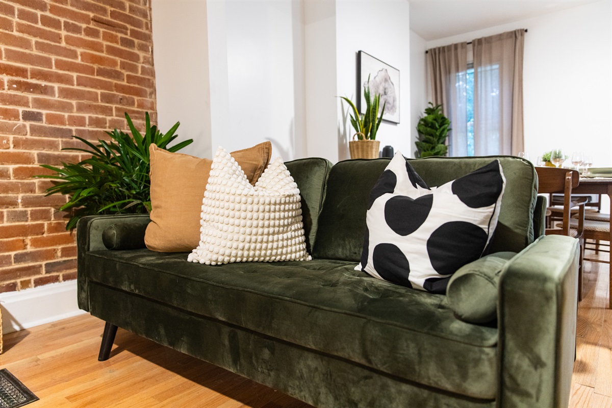 Velvet green loveseat with textured and patterned pillows set against a warm brick accent wall.