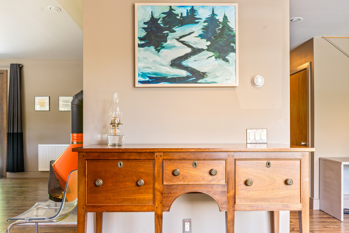 Eclectic warmth welcomes you to "The Crag." An antique wood sideboard features curated artwork, a traditional oil lamp, and a peek at the iconic orange cone fireplace anchored in the adjacent main living area.