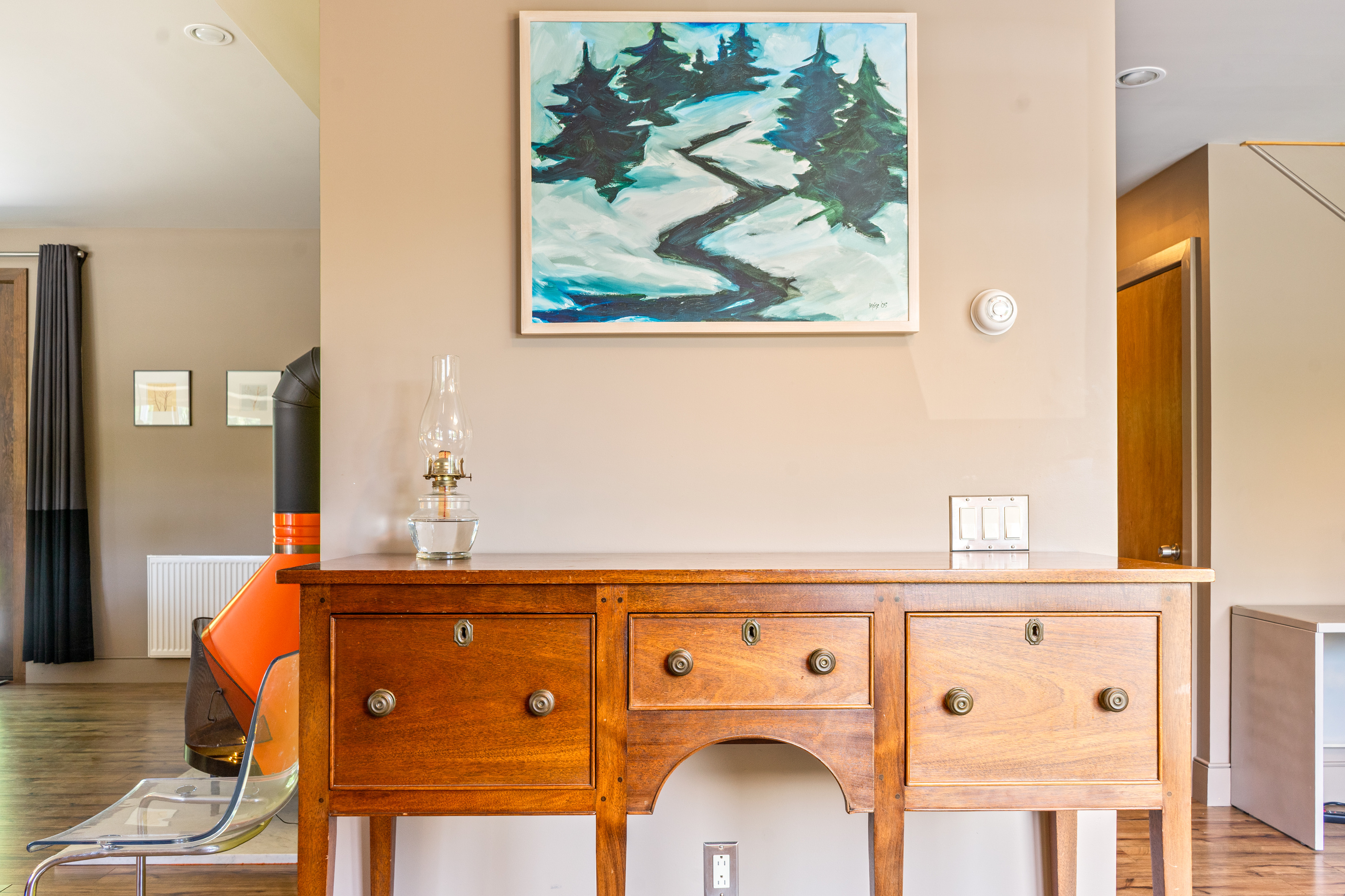 Eclectic warmth welcomes you to "The Crag." An antique wood sideboard features curated artwork, a traditional oil lamp, and a peek at the iconic orange cone fireplace anchored in the adjacent main living area.