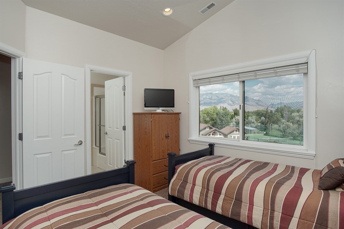 Bright and inviting, this twin bedroom features large windows that bring in natural light and frame picturesque mountain surroundings.