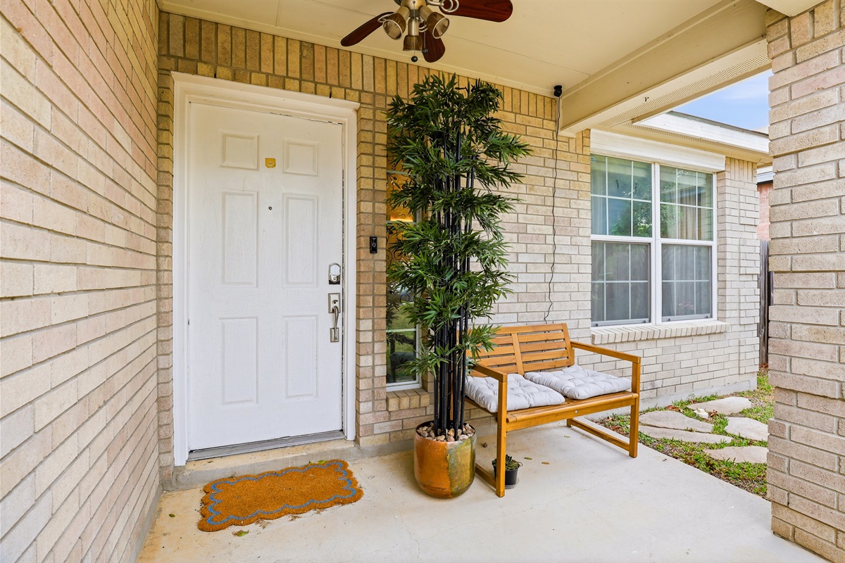 Covered private front entry with keyless smart lock, ceiling fan, wood bench, and welcome mat. Private and well-lit — your check-in code arrives before you do. No waiting and no keys needed!