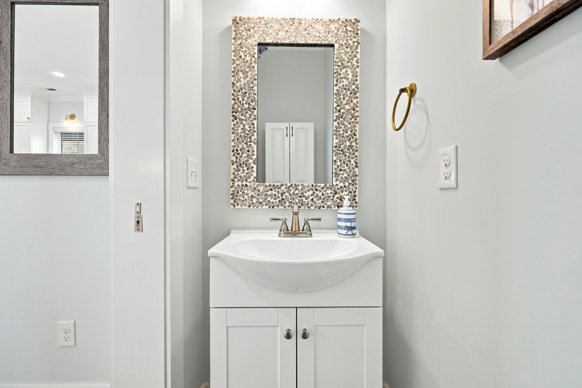 A charming and convenient half bathroom located on the top floor, featuring a clean coastal design with a bright vanity, decorative mirror, and modern finishes