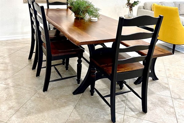 A Daning area with a Acacia wood table, 4 chairs and one bench that can seat up to 7 people. Abstract painting on the wall, light-Colored tiles and Off-white walls.