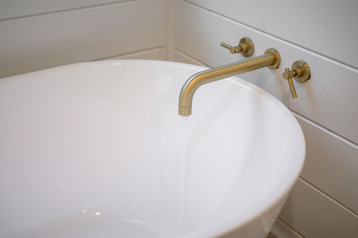 The elegant brushed brass tub filler adds a warm, modern touch to the freestanding soaking tub.