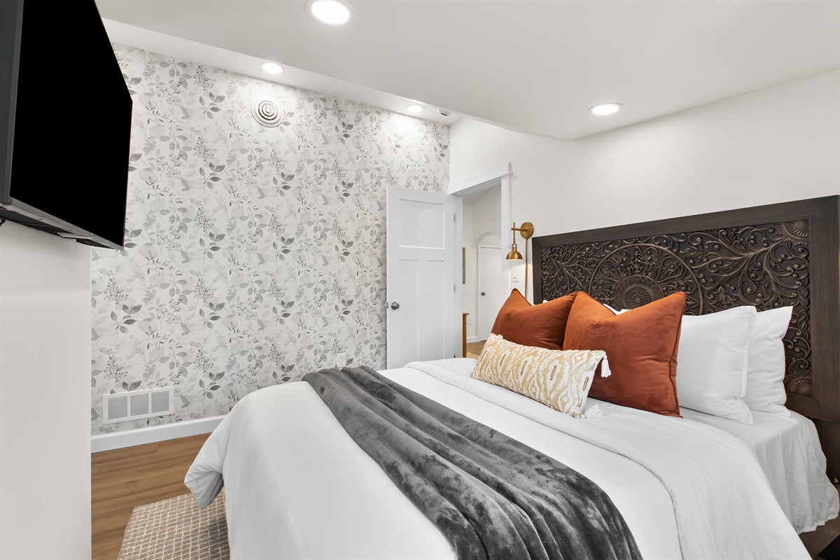 Elegant bedroom featuring bold accent wallpaper, plush bedding, and a wall-mounted smart TV.