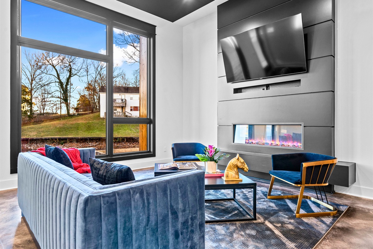 A cozy yet elegant living area, highlighted by deep blue accents and floor-to-ceiling windows that beautifully frame the surrounding landscape.