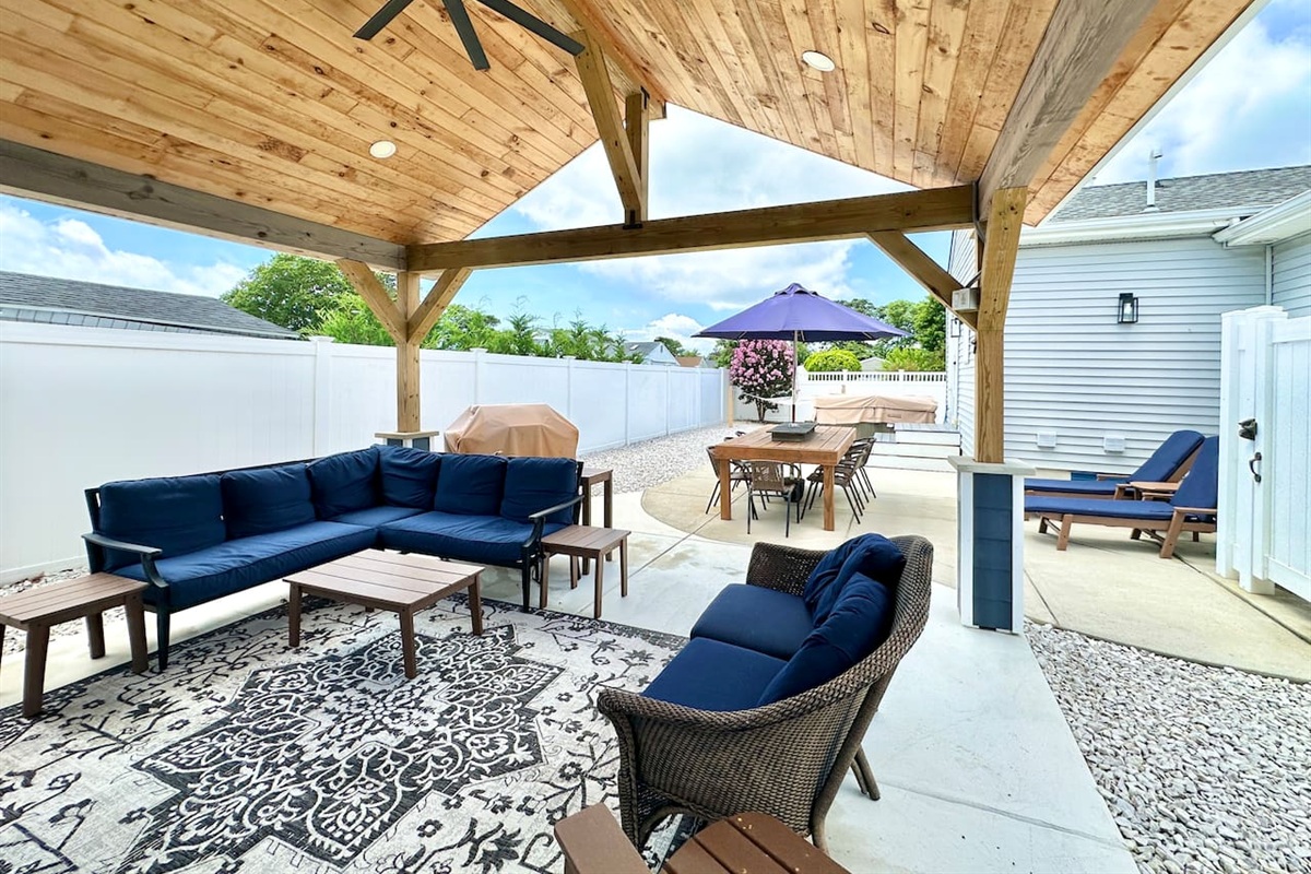 Relax under this impressive wooden pavilion, featuring navy sectional seating and a patterned rug. The space overlooks the hot tub, outdoor dining area, and professional grill for all-day entertainment.