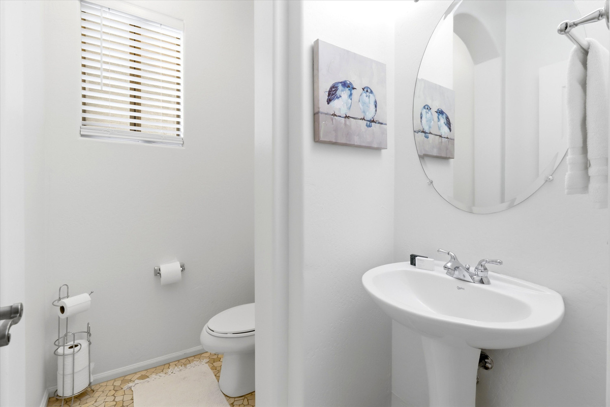 Half bathroom with a pedestal sink, round mirror, and a simple setup for guest use.

