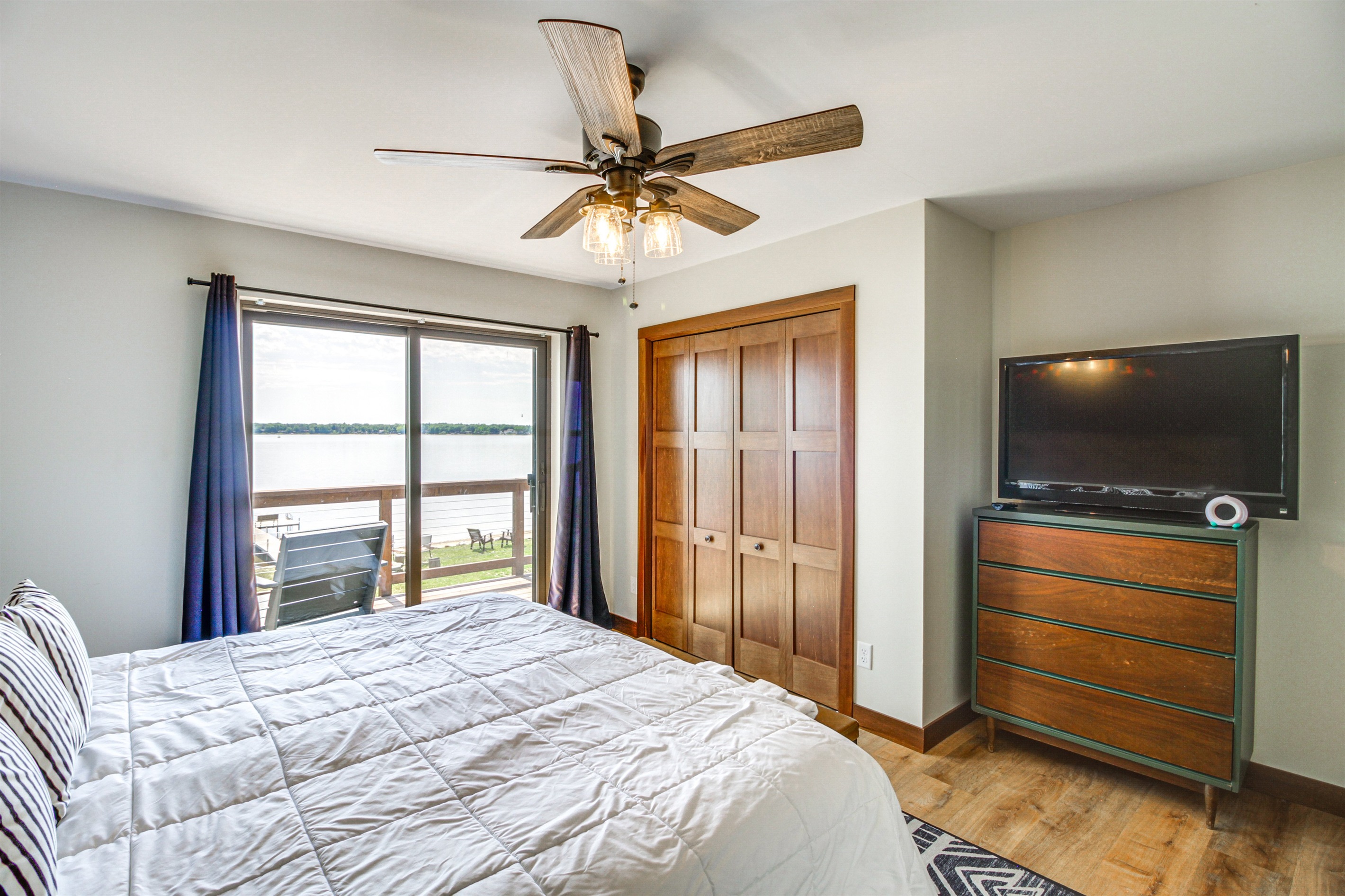 Primary bedroom with lake views, dresser, TV, and private deck access