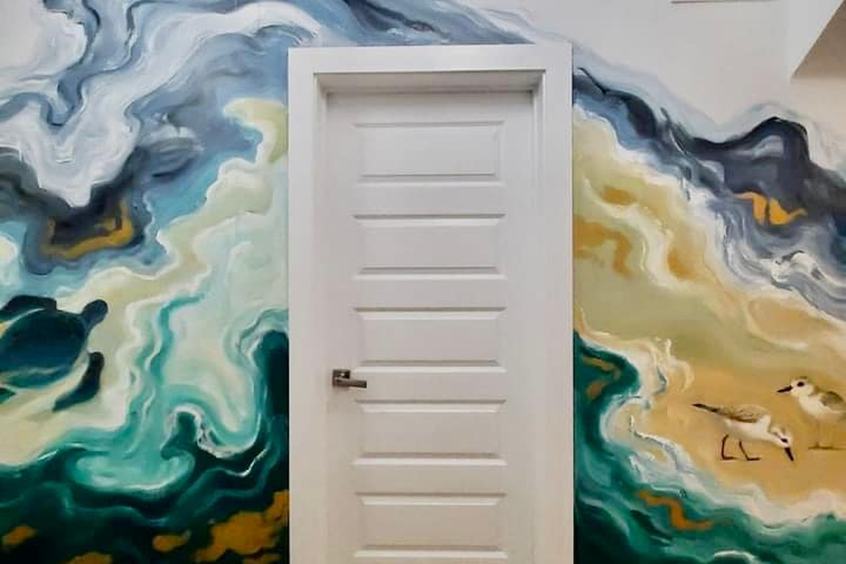 The mural carries upstairs too, wrapping the landing wall in green water and pale sand, with two sandpipers working the tideline. Small hands will find them first, though you will notice them by the third day.