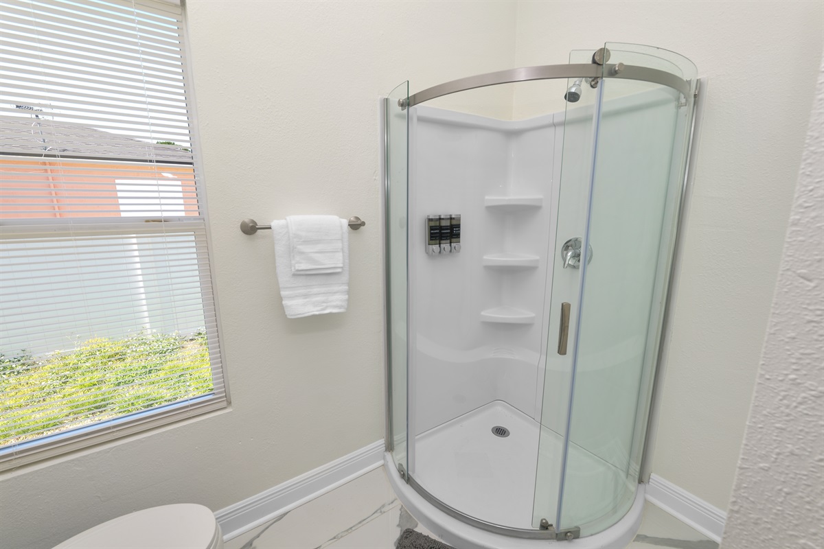 Compact yet stylish, this bathroom features a sleek glass-enclosed corner shower with built-in shelves and premium soap dispensers—ideal for a refreshing rinse after a day of adventure.