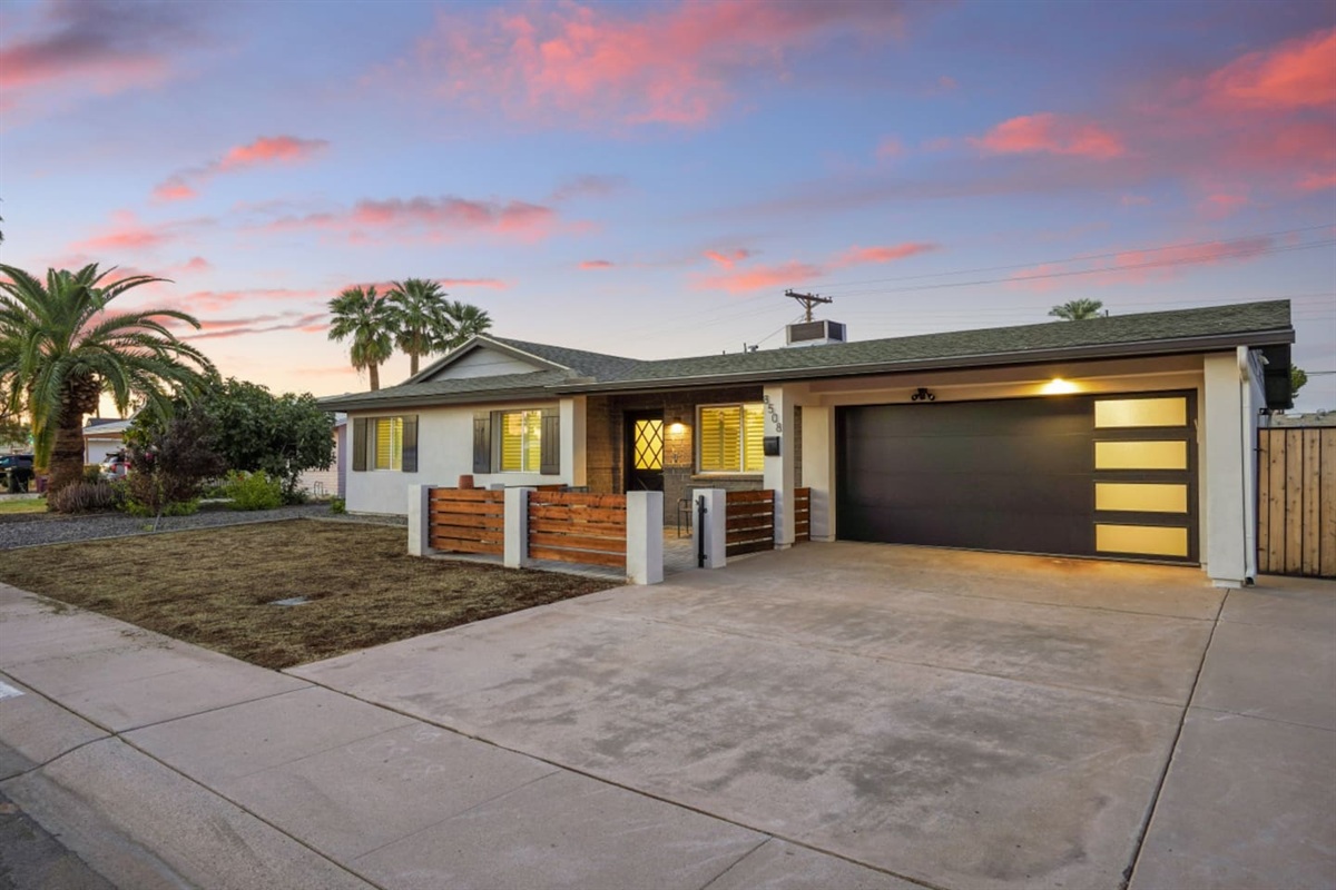 Front exterior at sunset with garage parking, paved driveway, and a welcoming patio entry.