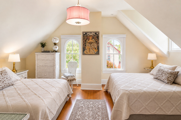 The third floor queen bedroom — vaulted ceilings, arched windows, and an Alphonse Mucha print that looks like it’s always lived here.