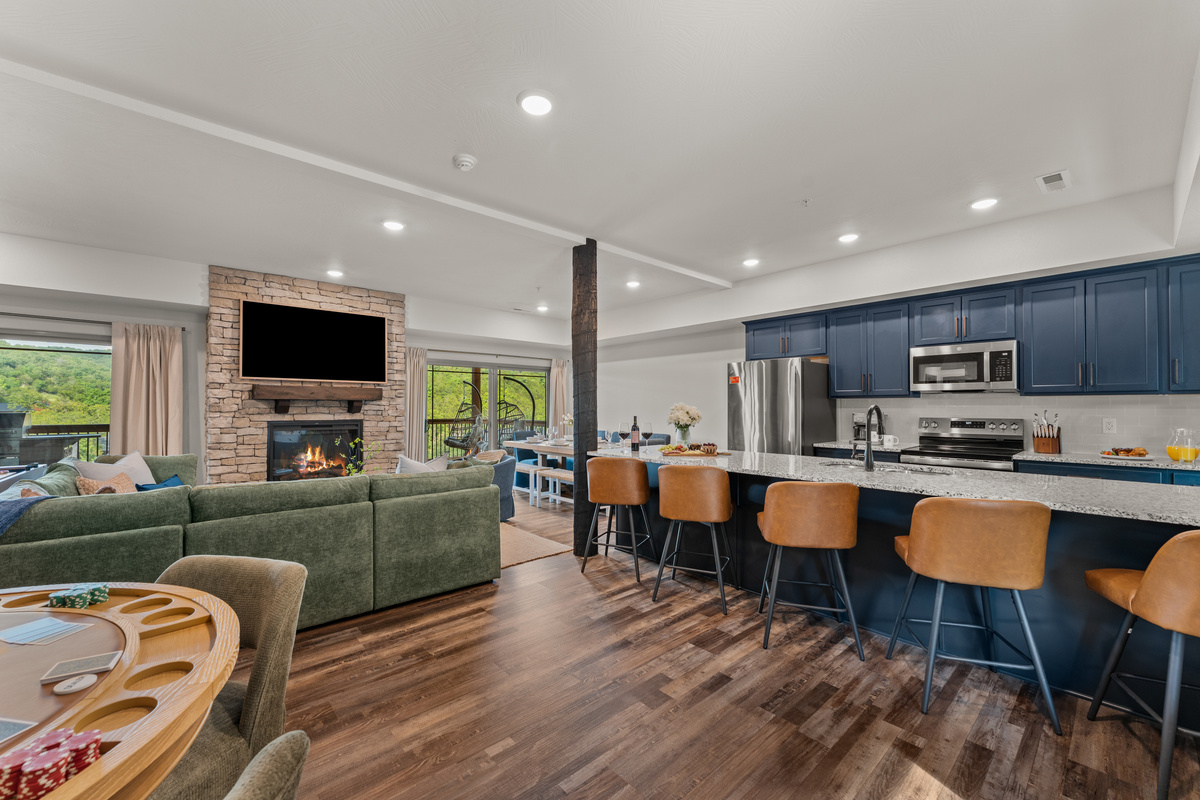 Gather in the bright, open-concept living and kitchen with a green sectional, stone gas fireplace, and a navy island that seats the whole group.