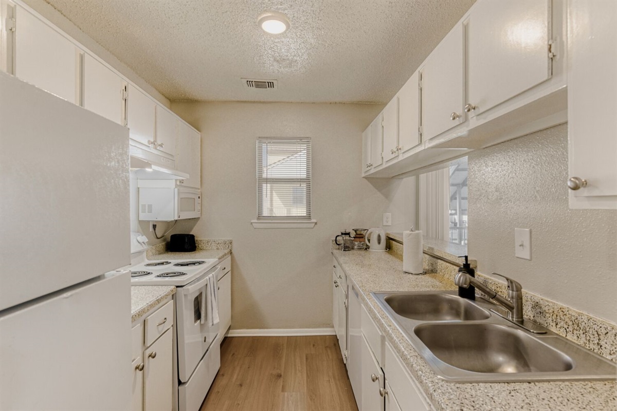A bright and functional galley kitchen featuring sleek white cabinetry, modern appliances, and warm wood flooring for a clean, inviting look.