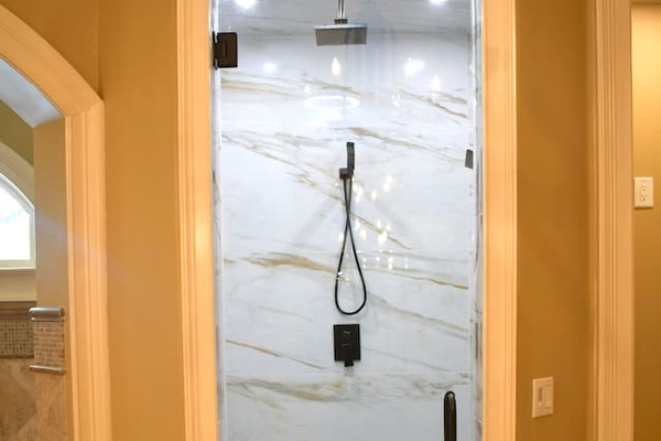Master bathroom with modern walk-in shower featuring frameless glass, marble-look tile walls, pebble floor, rainfall showerhead, handheld wand, built-in bench, recessed lighting, and matte black fixtures.