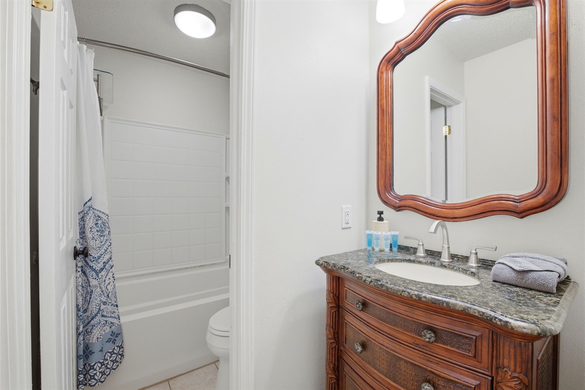 The bathroom includes a granite-topped vanity with a beautifully crafted wood cabinet and large framed mirror. With modern fixtures and a tub-shower combo, the space offers both comfort and functionality for guests.