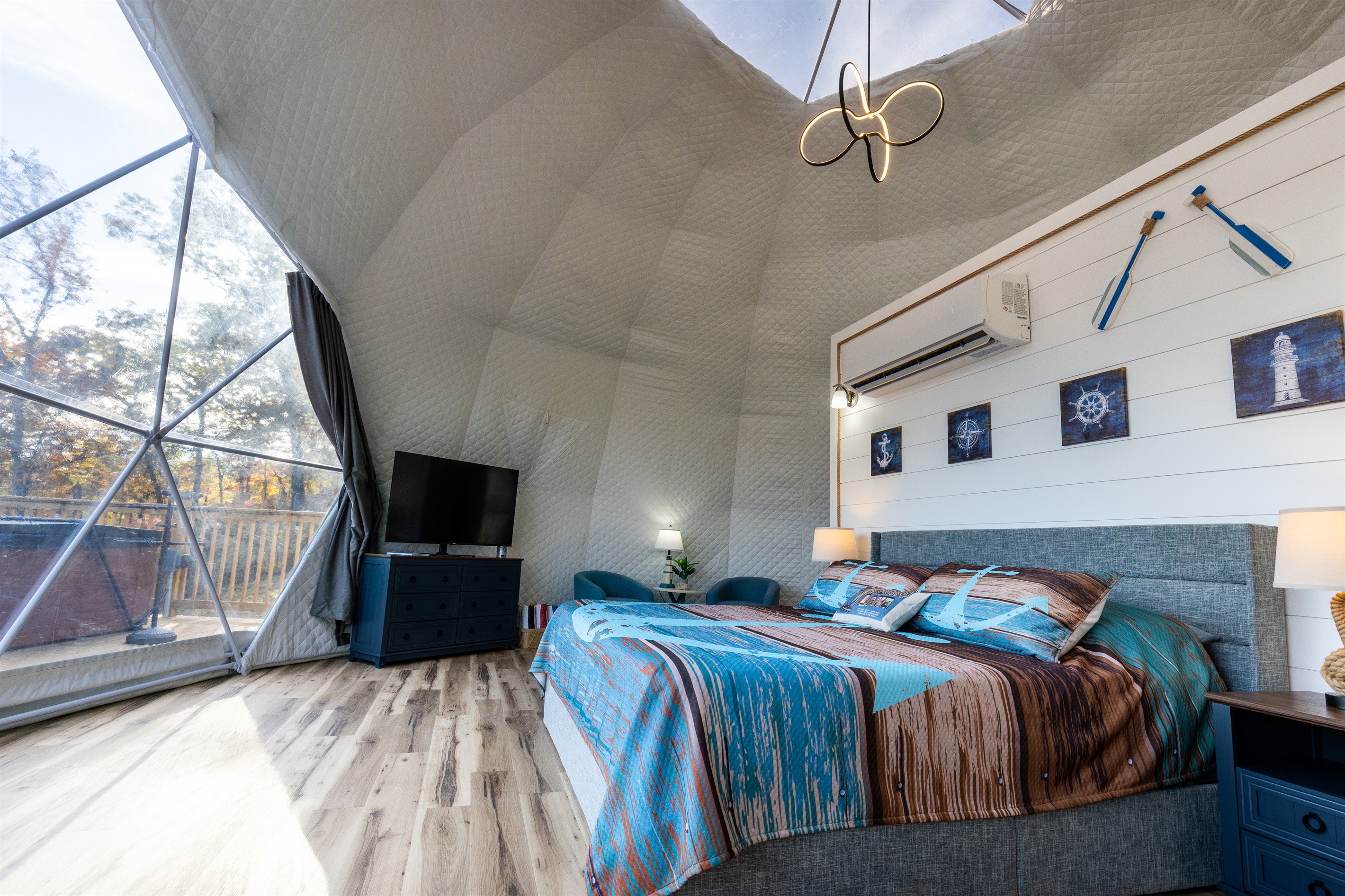 Spacious dome interior with king bed, cozy seating area, TV, and panoramic lake views through the massive bay window
